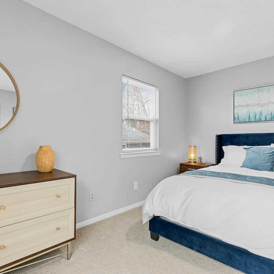 A repainted bedroom with a made bed, dresser and mirror.