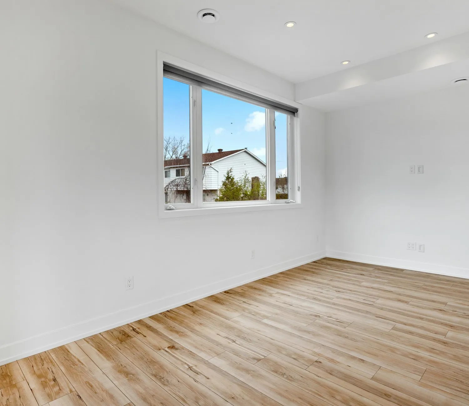 A repainted room with bare wood floors and a window looking onto a neighbouring house