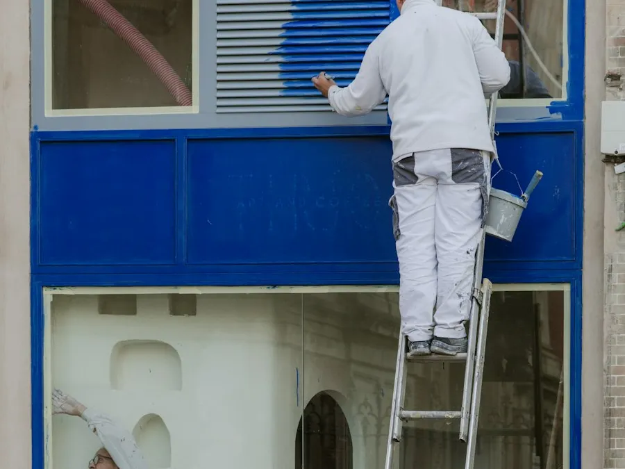 A painter working on the trim around an exterior window from a ladder.