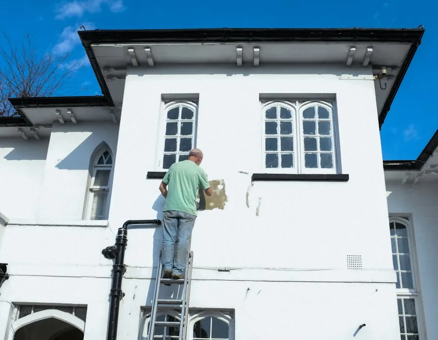 A painter cutting in the upper storey of a light-coloured house exterior.